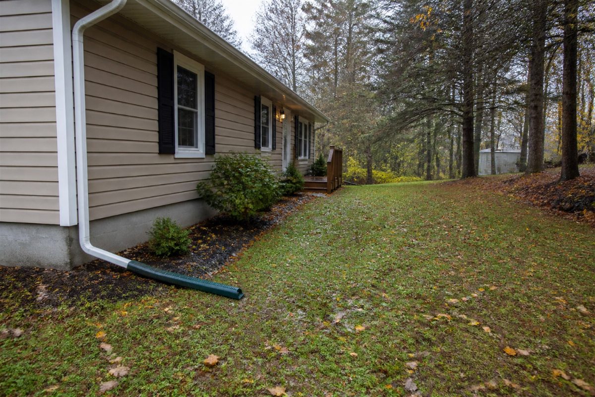 A downspout carries rainwater away from a home's foundation across a gently sloped yard.