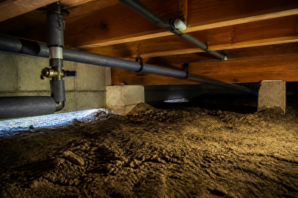 Water pipes in a crawl space covered with pipe insulation near the foundation.