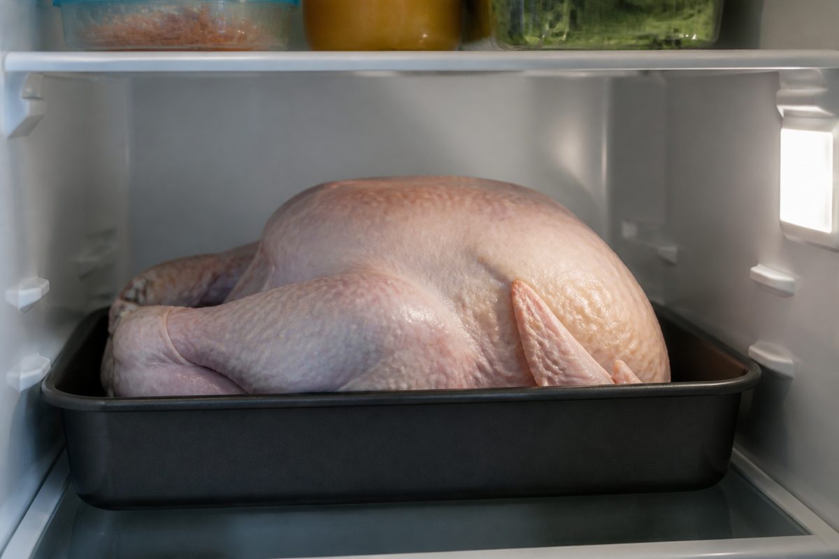 A raw turkey placed in a container on a refrigerator shelf to prevent dripping.