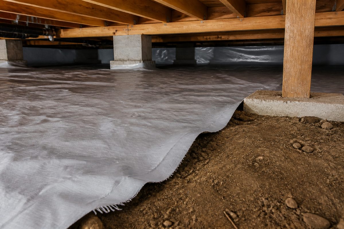 A crawl space vapor barrier with an exposed patch of soil that can be checked for ground moisture.