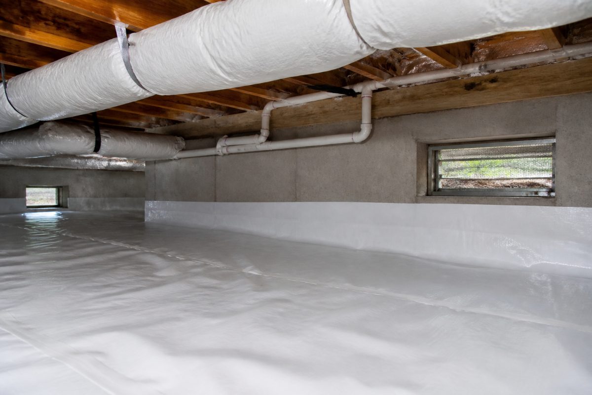 A crawl space with insulated pipes and a ground vapor barrier along the floor.