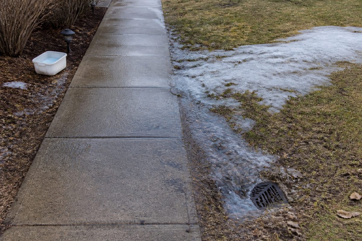 Meltwater and a small icy patch are visible beside a residential walkway.