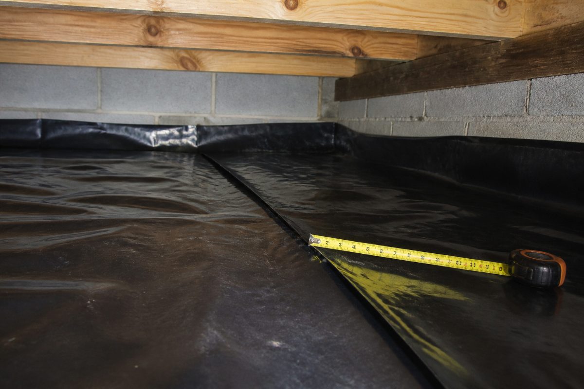 A tape measure is placed beside an overlapping seam in a crawl space liner.
