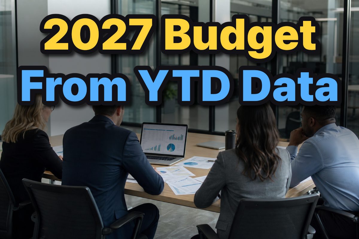 A business finance team reviews a 2027 budget forecast using a laptop and printed spreadsheets.