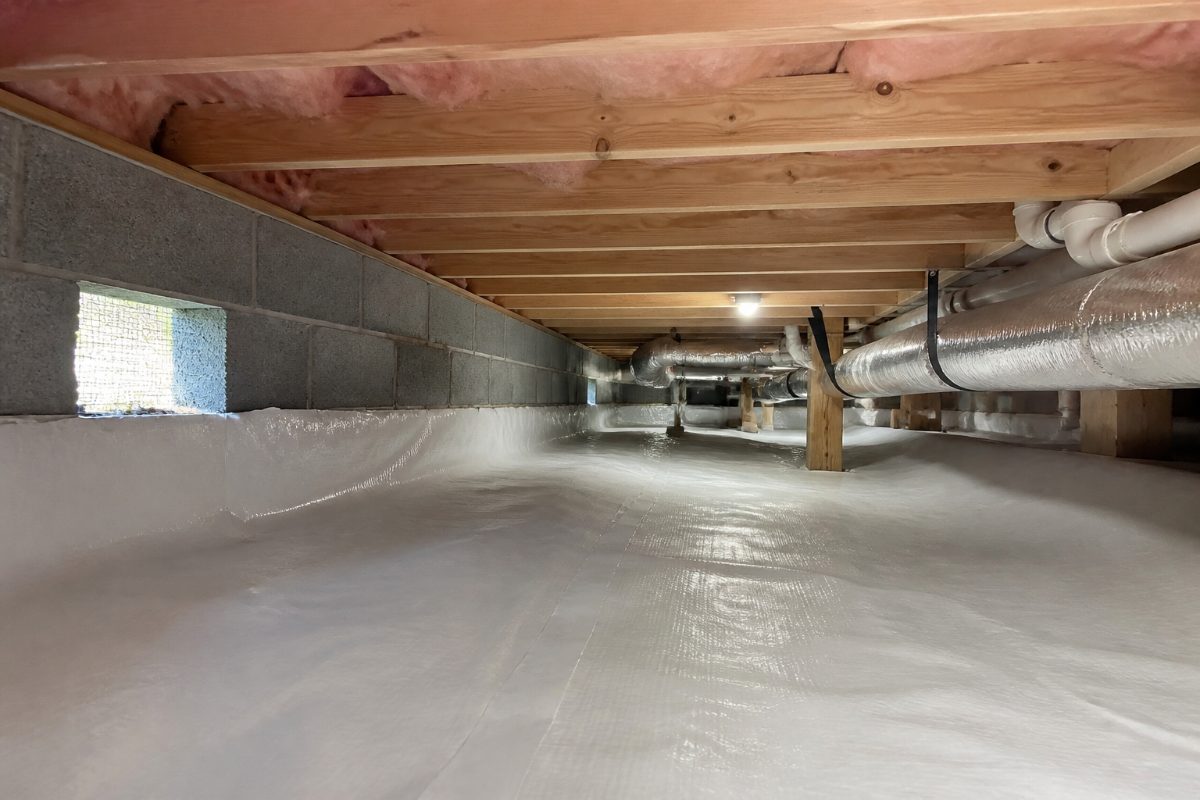 A residential crawl space showing a foundation vent, floor joists, and plumbing.