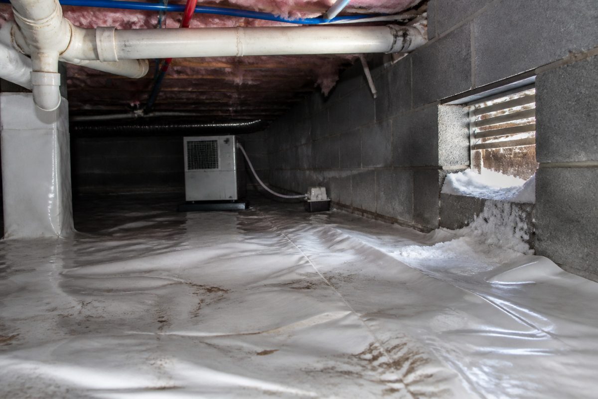 A crawl space with plumbing and a dehumidifier used as part of moisture management.
