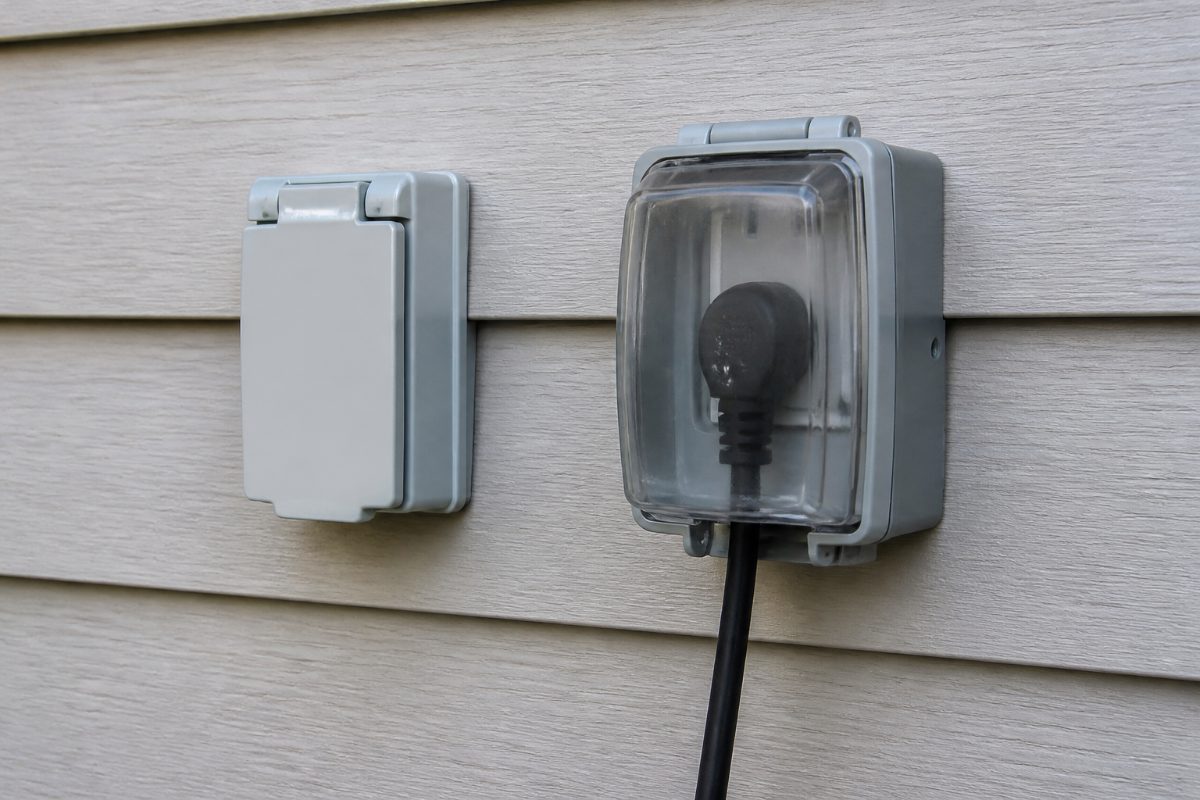 A basic outlet cover beside an in-use cover enclosing a connected Christmas-light plug.