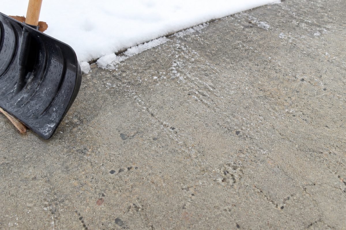 A few rock-salt crystals rest on a weathered concrete driveway beside a shovel.